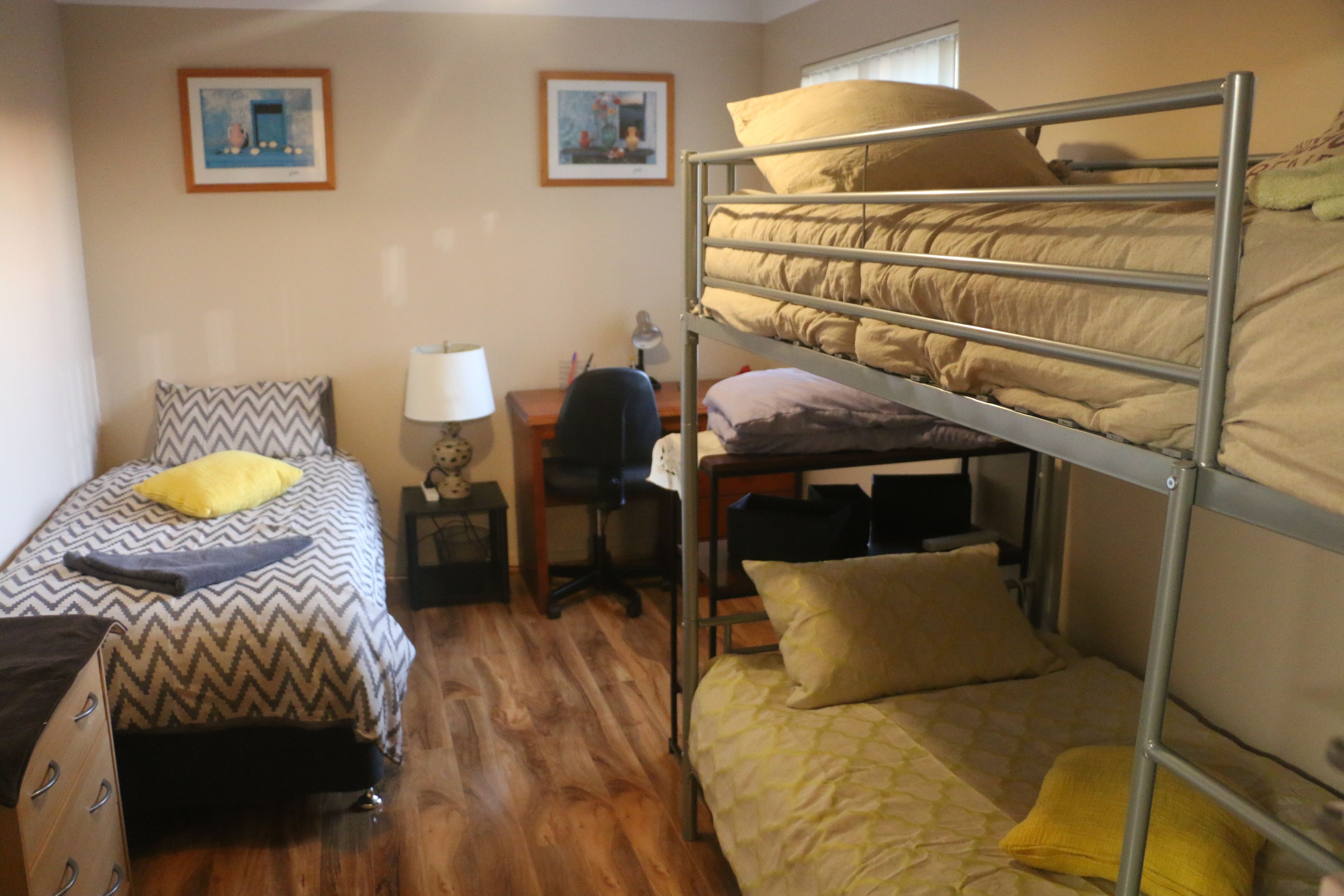 Una habitación tipo dormitorio con literas, un escritorio, una silla y dos cuadros en la pared.