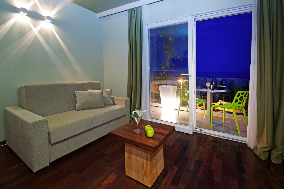 A living room with a sofa, a wooden coffee table, and a view of a balcony with outdoor seating.