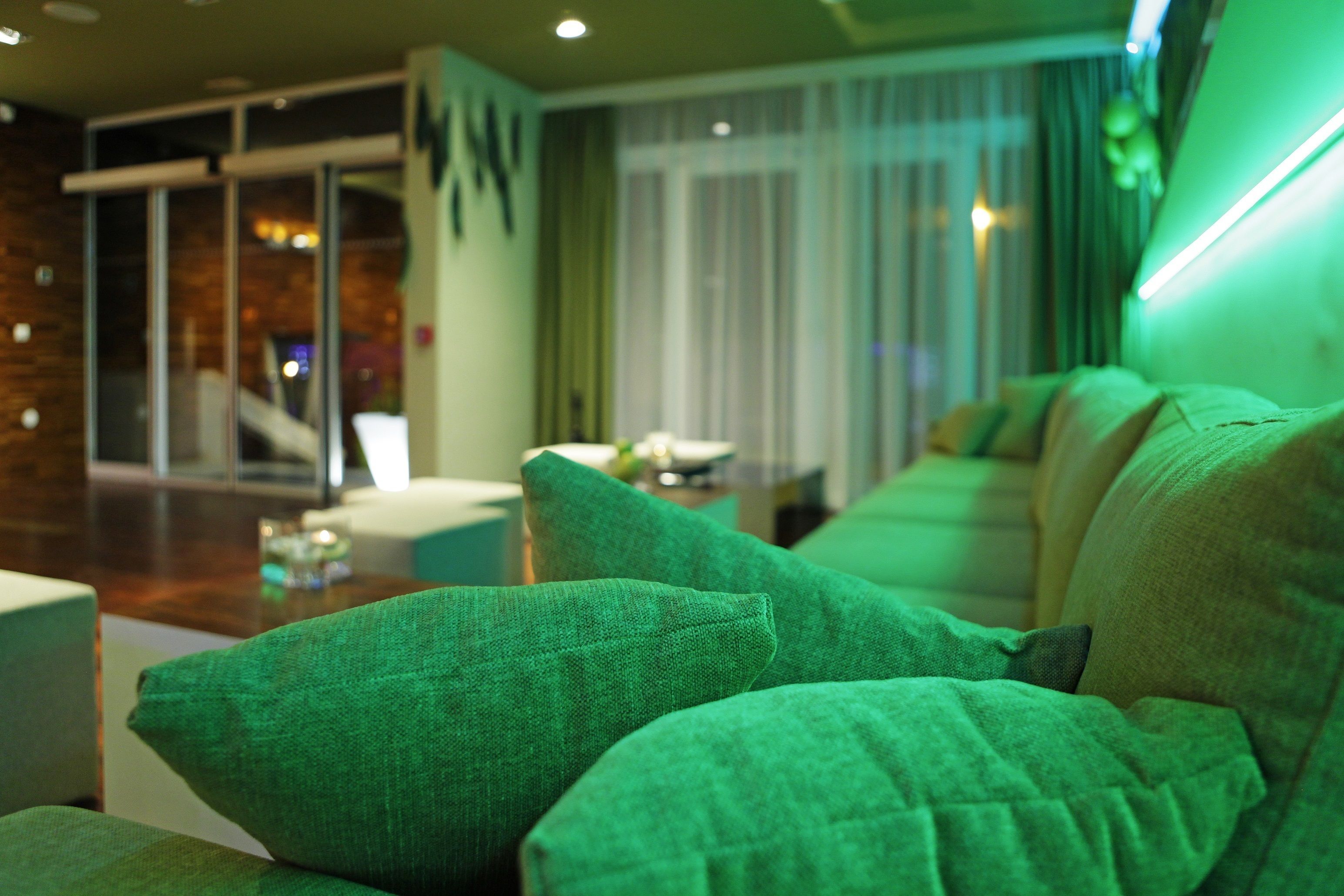 A modern living room with a green sofa, a wooden coffee table, and a large window with curtains.
