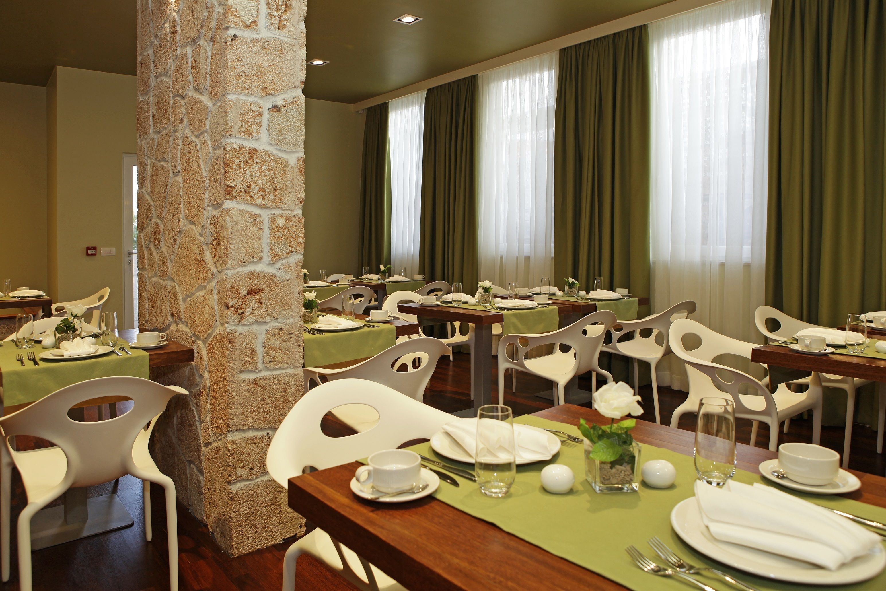 A dining area with multiple tables set for meals, white chairs, and a stone pillar.