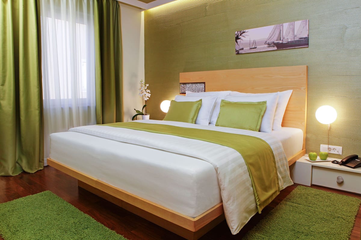 A neatly made bed with a green and white bedspread, a wooden headboard, and a nightstand with a lamp and a phone.