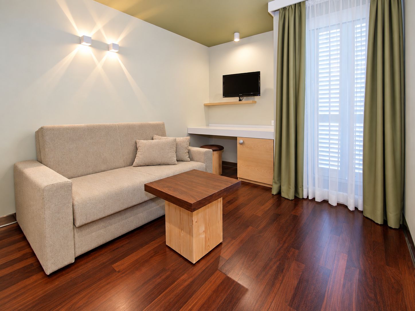 A modern living room with a sofa, a wooden coffee table, a flat-screen TV, and a window with curtains.