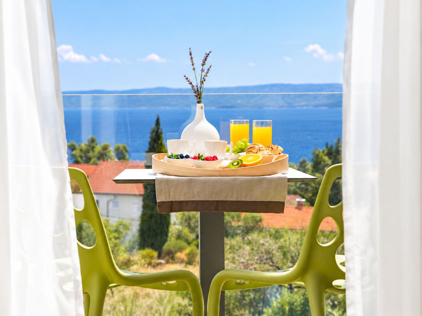 A table with breakfast items and two glasses of orange juice, set against a scenic view of the sea and mountains.