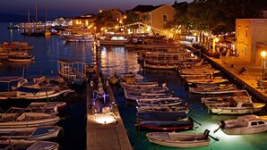 A marina at dusk with boats docked, a pier, and buildings with lights. - Boutique Hotel Bol (Bol)