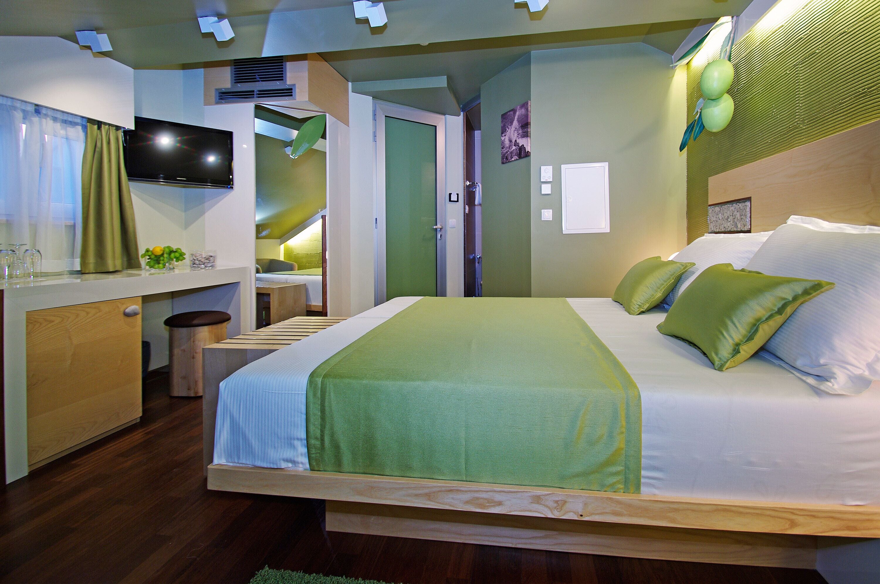 Ein modernes Hotelzimmer mit einem großen Bett, einem Fernseher, einem kleinen Schreibtisch und einem durchgegangenen Tür einsehbaren Badezimmer.