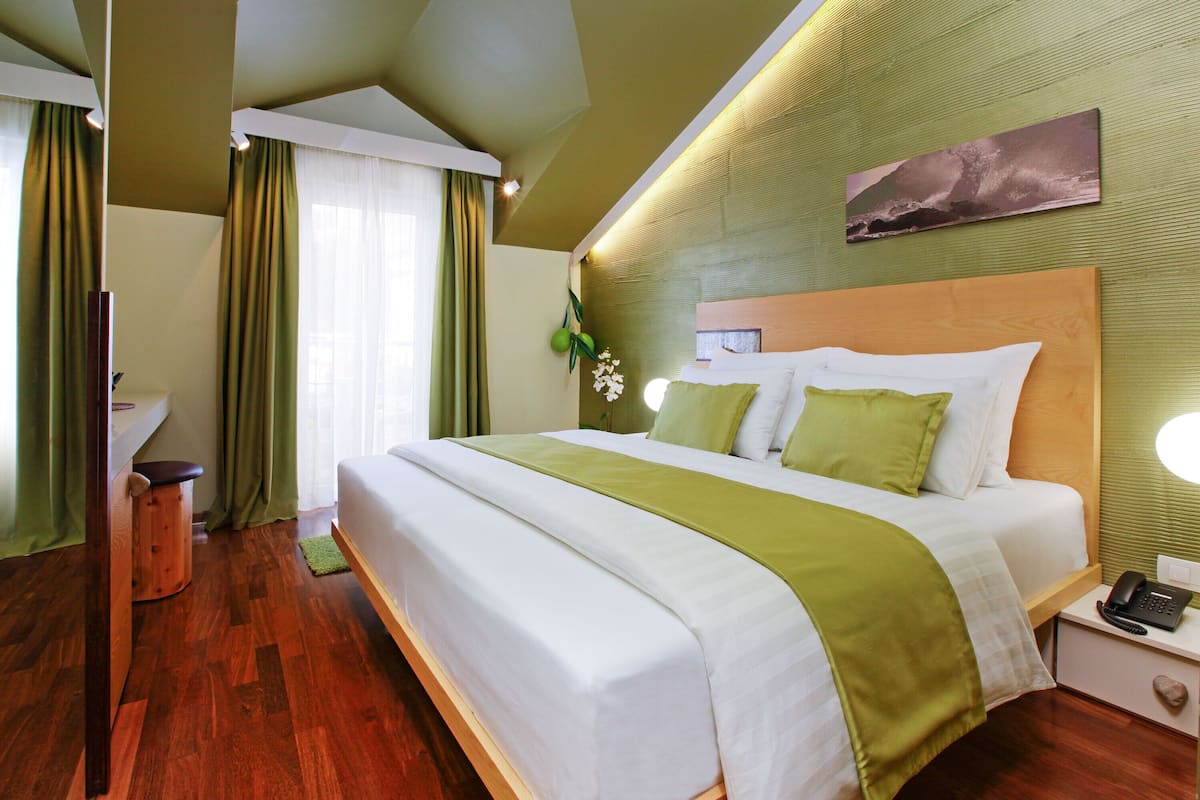 A hotel room with a large bed, a bedside table with a phone, a mirror, and a green curtain.