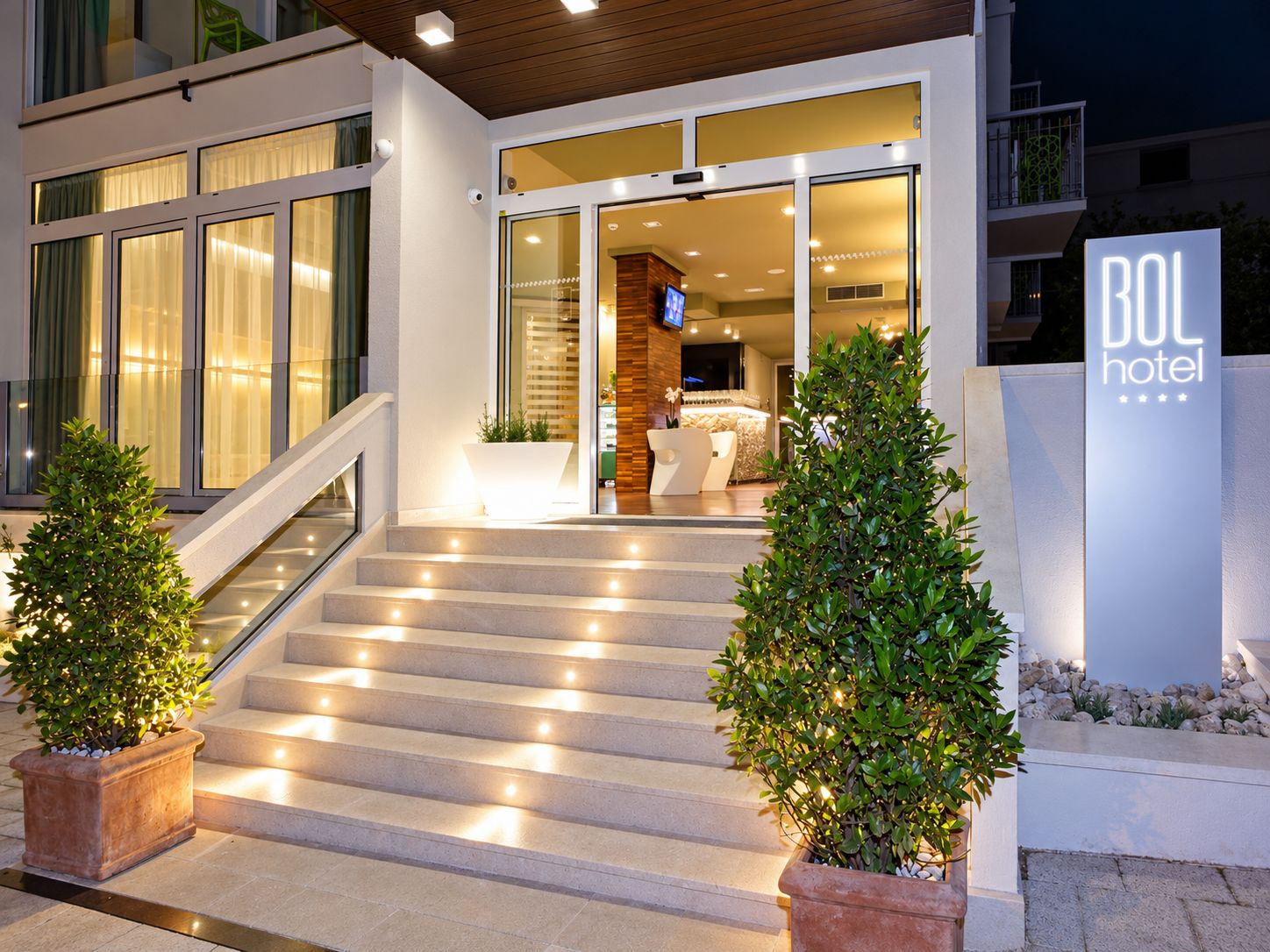 A hotel entrance with a staircase, potted plants, and a sign indicating the hotel name.
