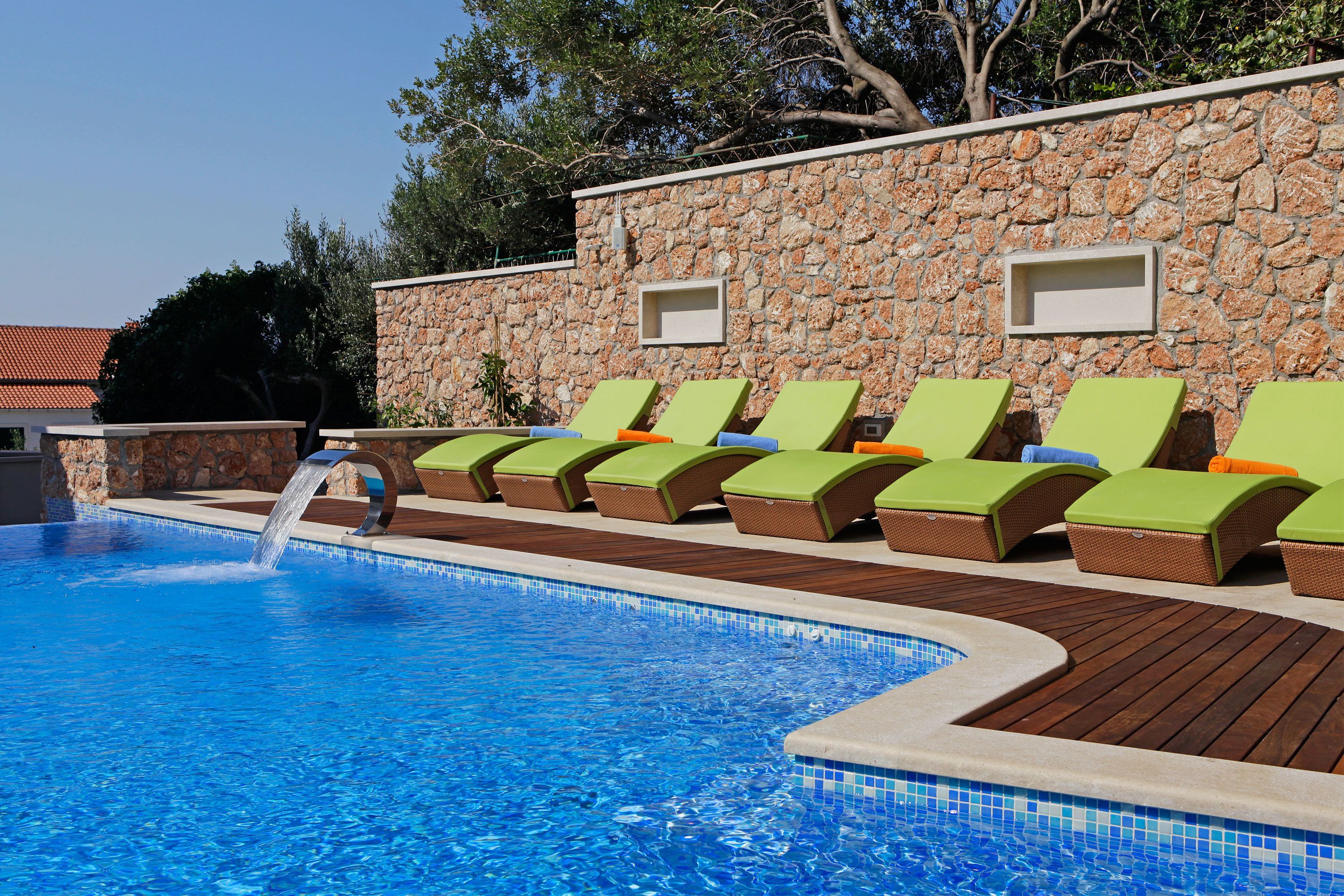 A swimming pool with a stone wall and lounge chairs.