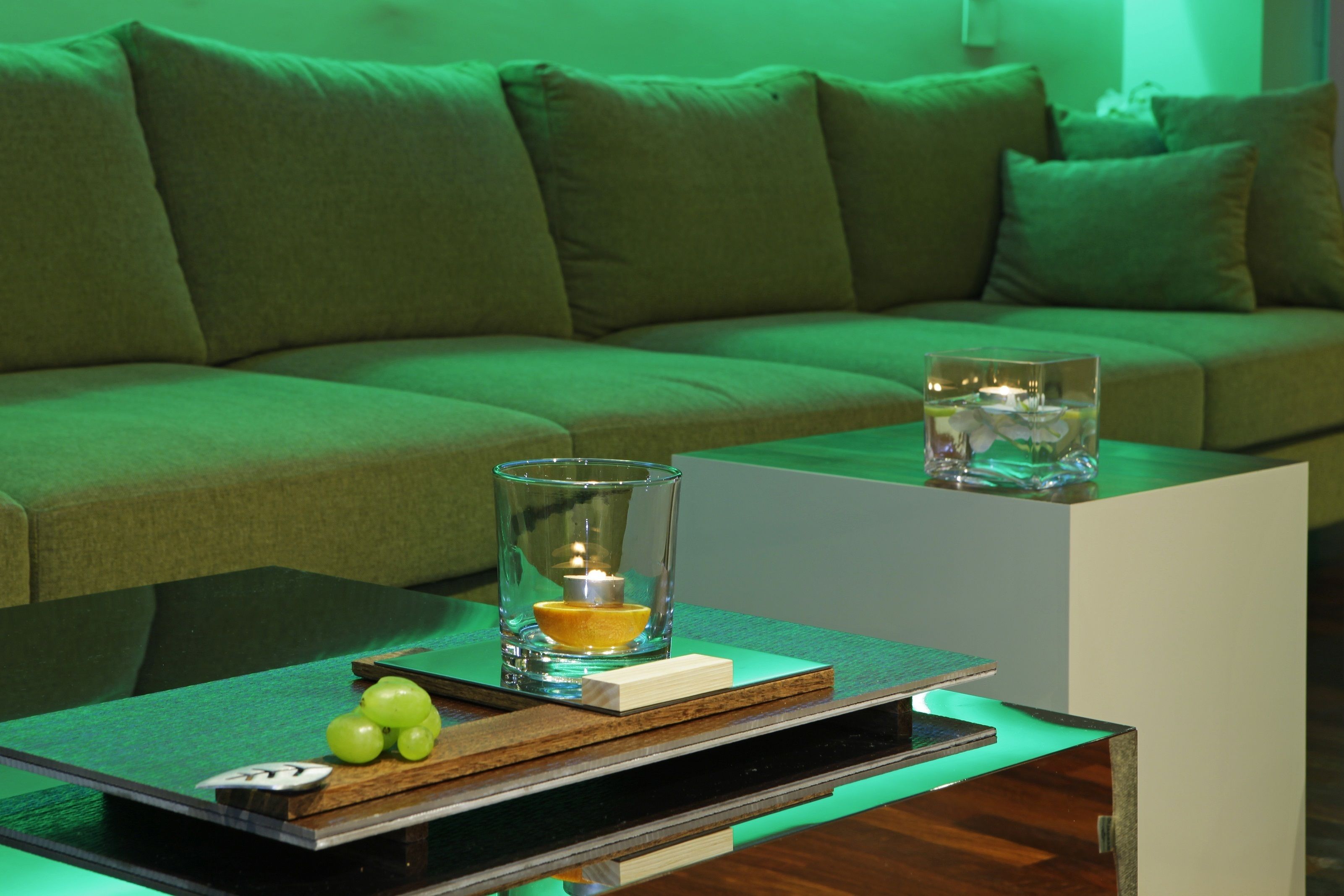 Una sala de estar moderna con un sofá verde, una mesa de vidrio con una vela y un libro.