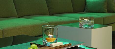 Una sala de estar moderna con un sofá verde, una mesa de vidrio con una vela y un libro.