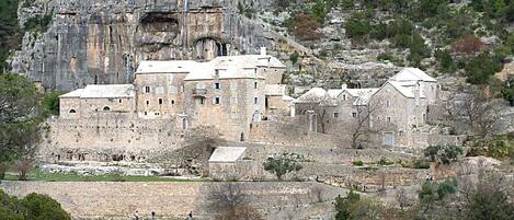 A historic stone building with multiple levels and a fortified entrance, surrounded by rocky terrain and sparse vegetation.