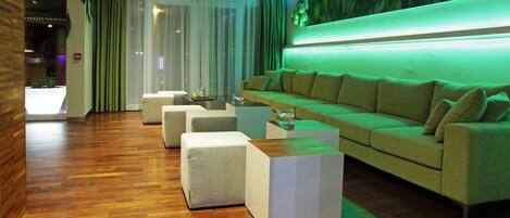 A modern living room with a green-lit wall, a beige sofa, and white ottomans.