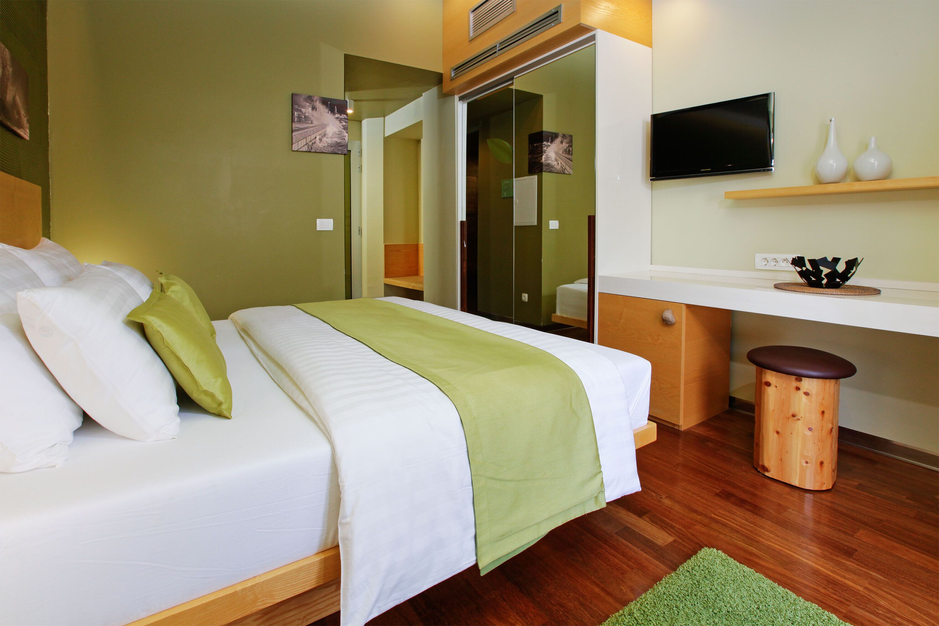 Ein Hotelzimmer mit Bett, Schreibtisch, Fernseher und einem kleinen Hocker.