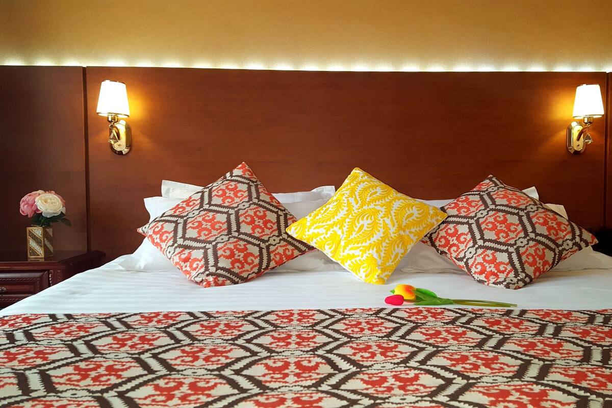 A hotel room with a large bed, patterned bedspread, and decorative pillows.