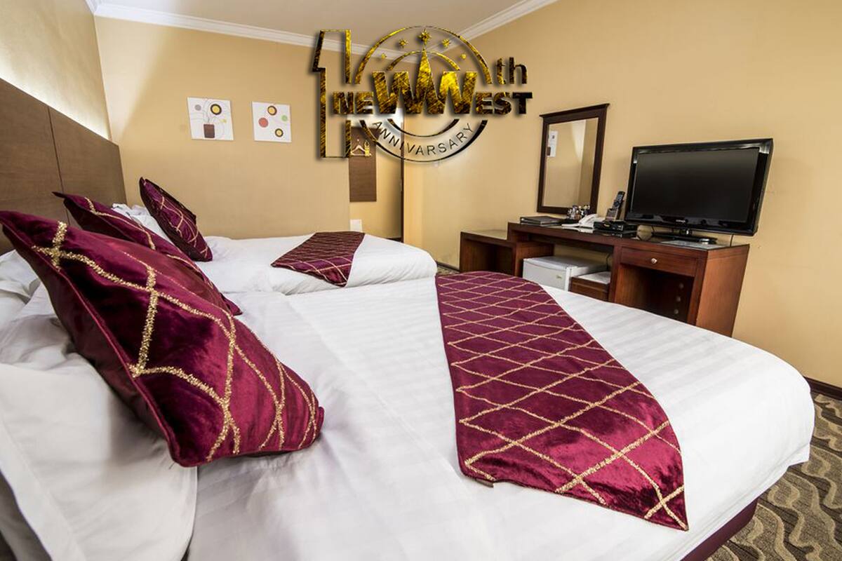 A hotel room with two beds, a desk, a television, and a mirror.