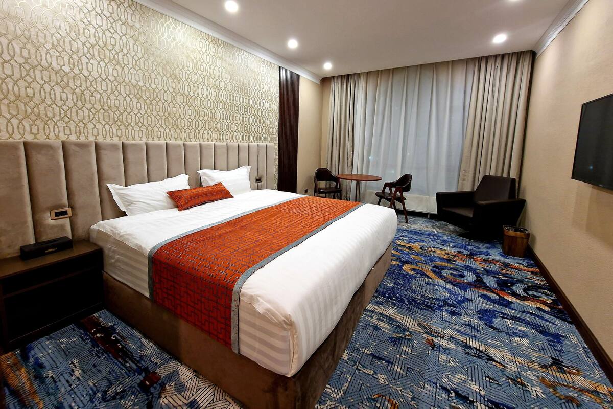 A hotel room with a large bed, a desk, a chair, and a TV.