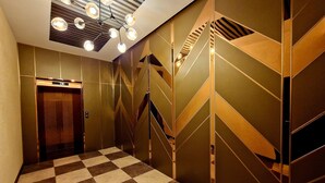 En hall med ett rutmönstrat golv, en träbeklädd hiss och en trappa med geometriska mönster på väggarna.