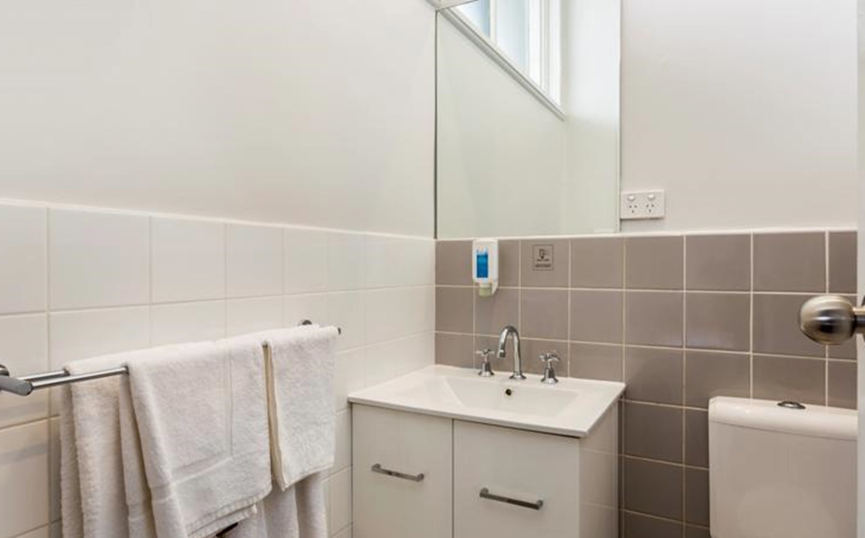 Un baño con lavamanos blanco, un espejo y un perchero para toallas.