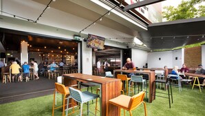 An outdoor dining area with wooden tables and metal chairs, surrounded by a grassy lawn. - Nightcap at Caringbah Hotel (Caringbah)