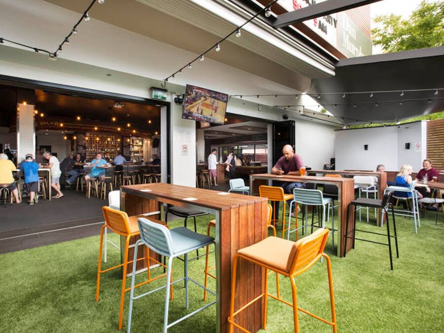 An outdoor dining area with wooden tables and metal chairs, surrounded by a grassy lawn.