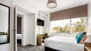 A hotel room with a bed, a desk, a TV, and a window with a view of palm trees. - Nightcap at Caringbah Hotel (Caringbah)