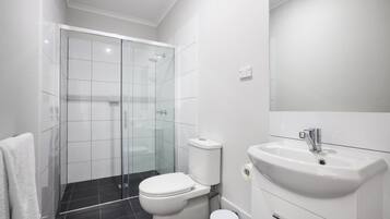 A modern bathroom with a glass shower enclosure, a white toilet, and a white sink with a mirror above it.