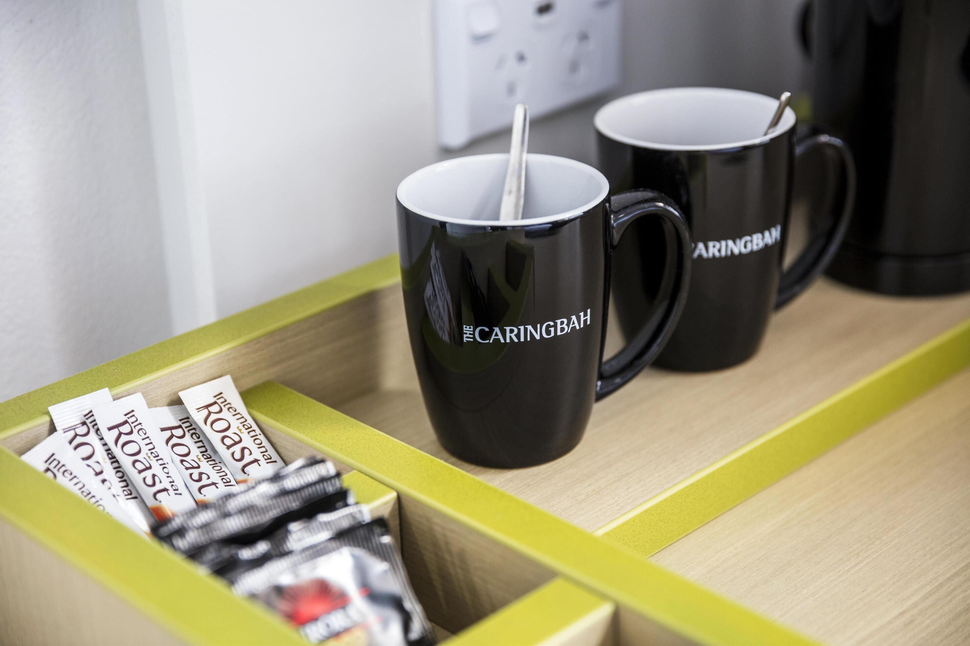 Una bandeja con dos tazas negras etiquetadas "The Caringbah" y una caja de sobres de "International Roast".