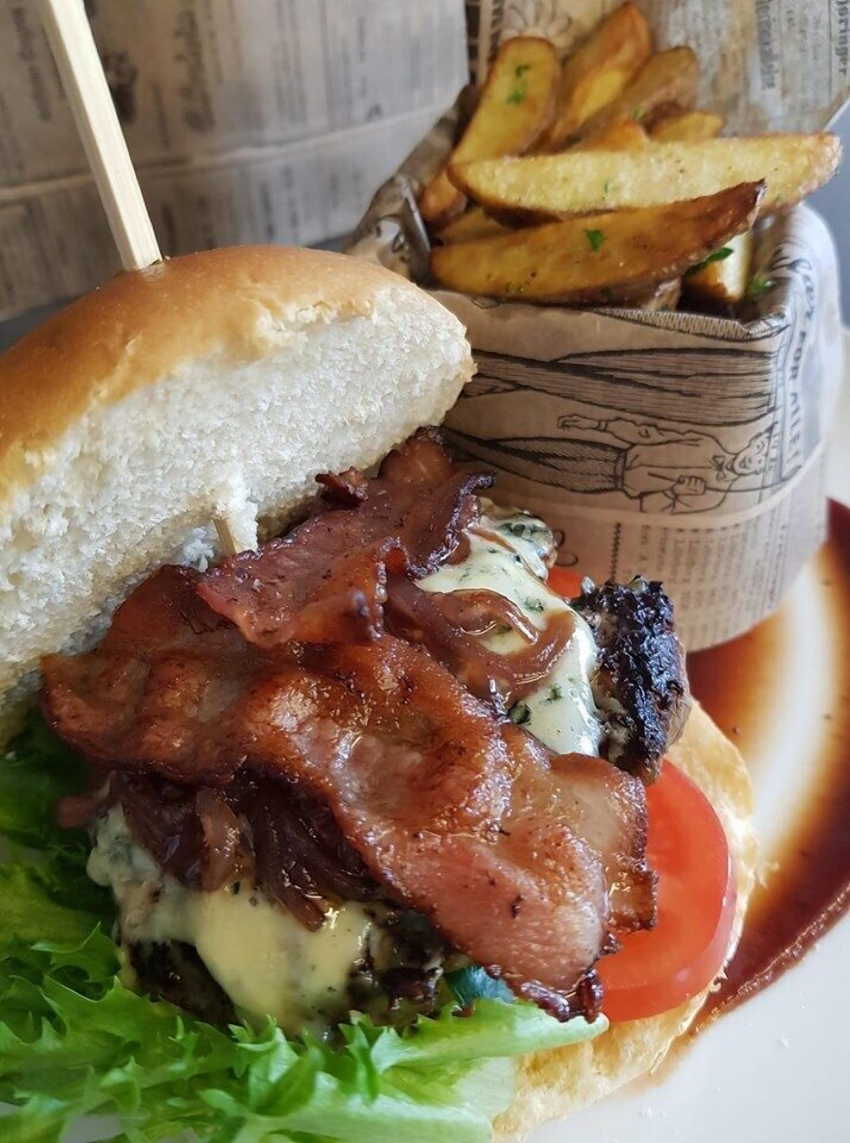 Un sandwich au bacon, au fromage et à la tomate, servi dans un pain, accompagné d’un panier de frites.