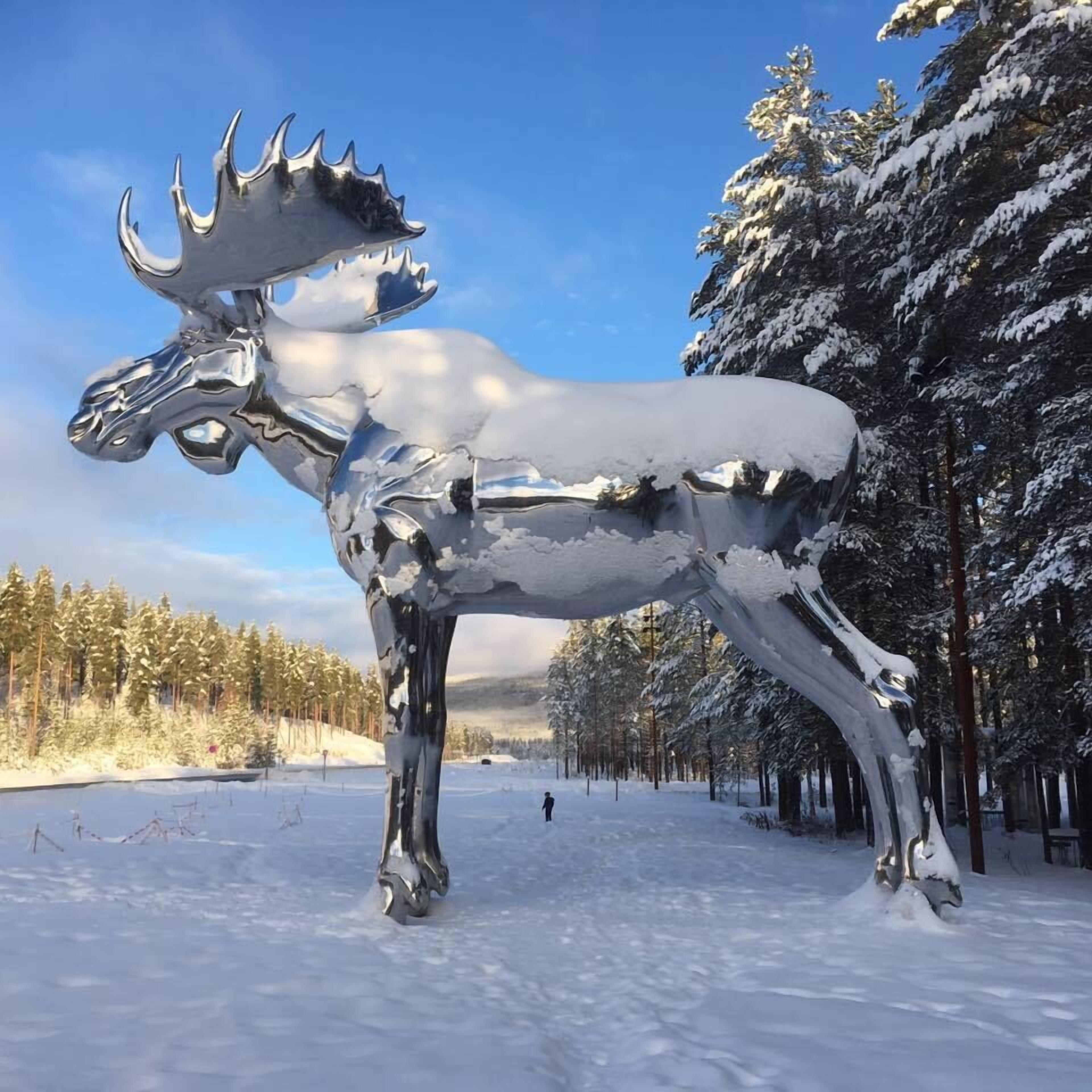 A large metallic moose sculpture in a snowy forest setting.