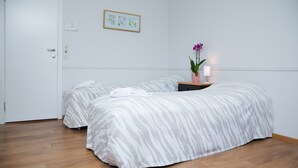 A room with two beds, a wooden floor, a small table with a lamp, and a framed picture on the wall. - Stor-Elvdal Hotell (Stor-Elvdal)