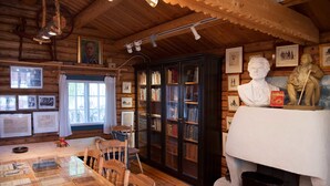 A wooden cabin interior with a dining table, chairs, bookshelves, and a fireplace. - Stor-Elvdal Hotell (Stor-Elvdal)