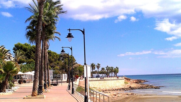 Une promenade en bord de mer, bordée de palmiers, d’éclairages publics et donnant sur une plage.