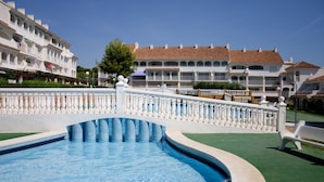 Une piscine bordée d’une balustrade blanche, entourée d’une pelouse verdoyante et de bâtiments blancs dotés de balcons.