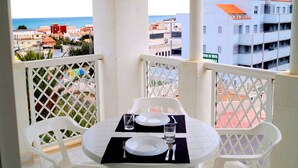 Un balcon avec une table dressée pour deux personnes, offrant une vue sur le paysage urbain de la côte.