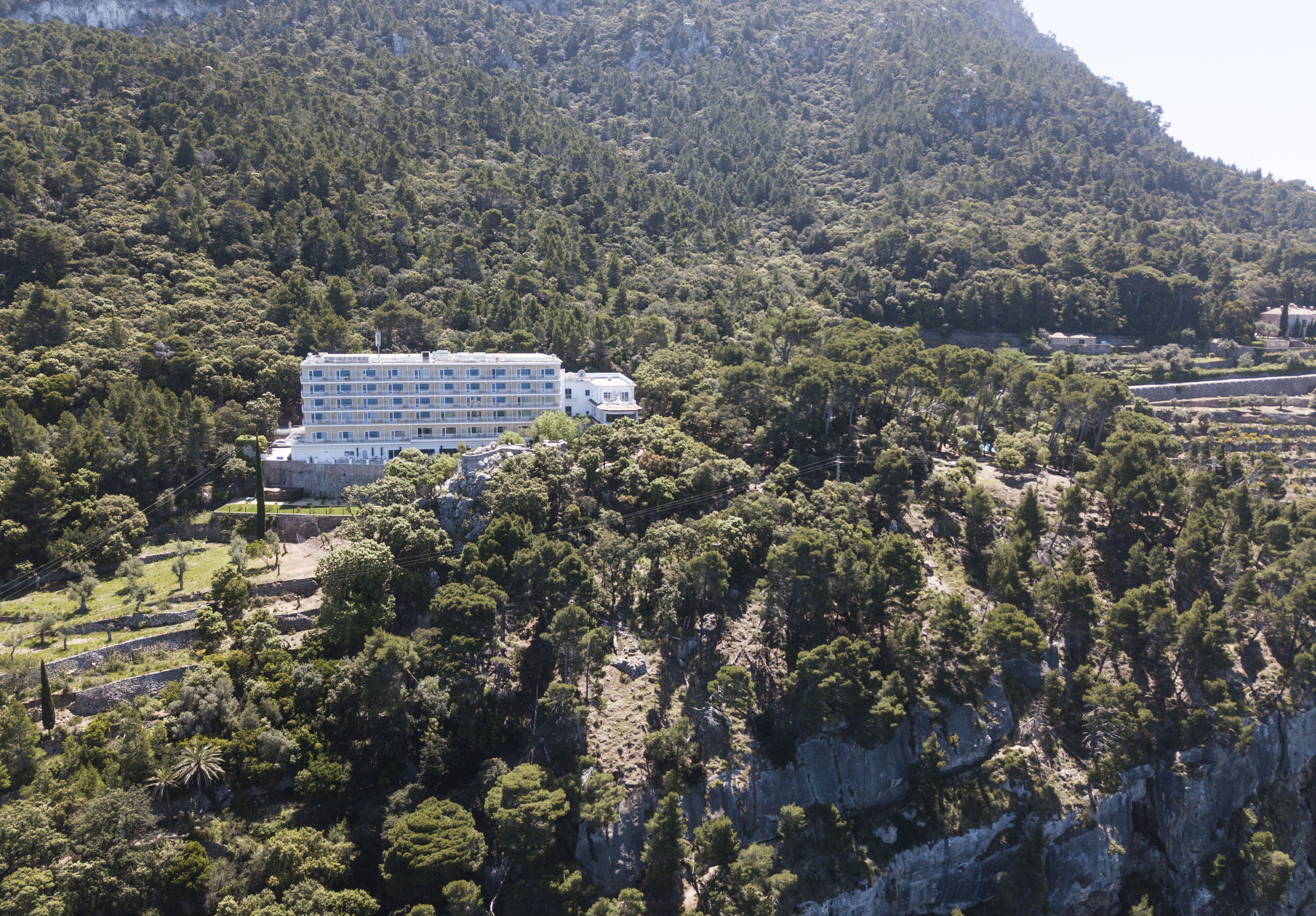A hotel with multiple floors, surrounded by dense forest and rocky terrain.