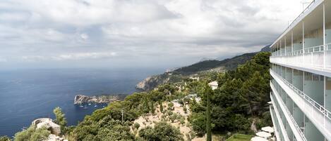 Un hôtel situé sur la côte, offrant une vue sur la mer et les montagnes. Il dispose d’un balcon avec un espace salon extérieur.