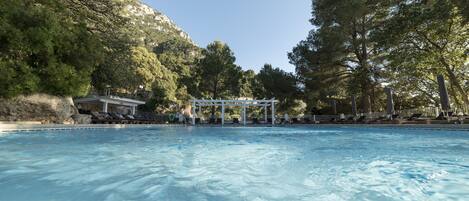 A swimming pool with a gazebo and lounge chairs, surrounded by trees and a mountain backdrop.