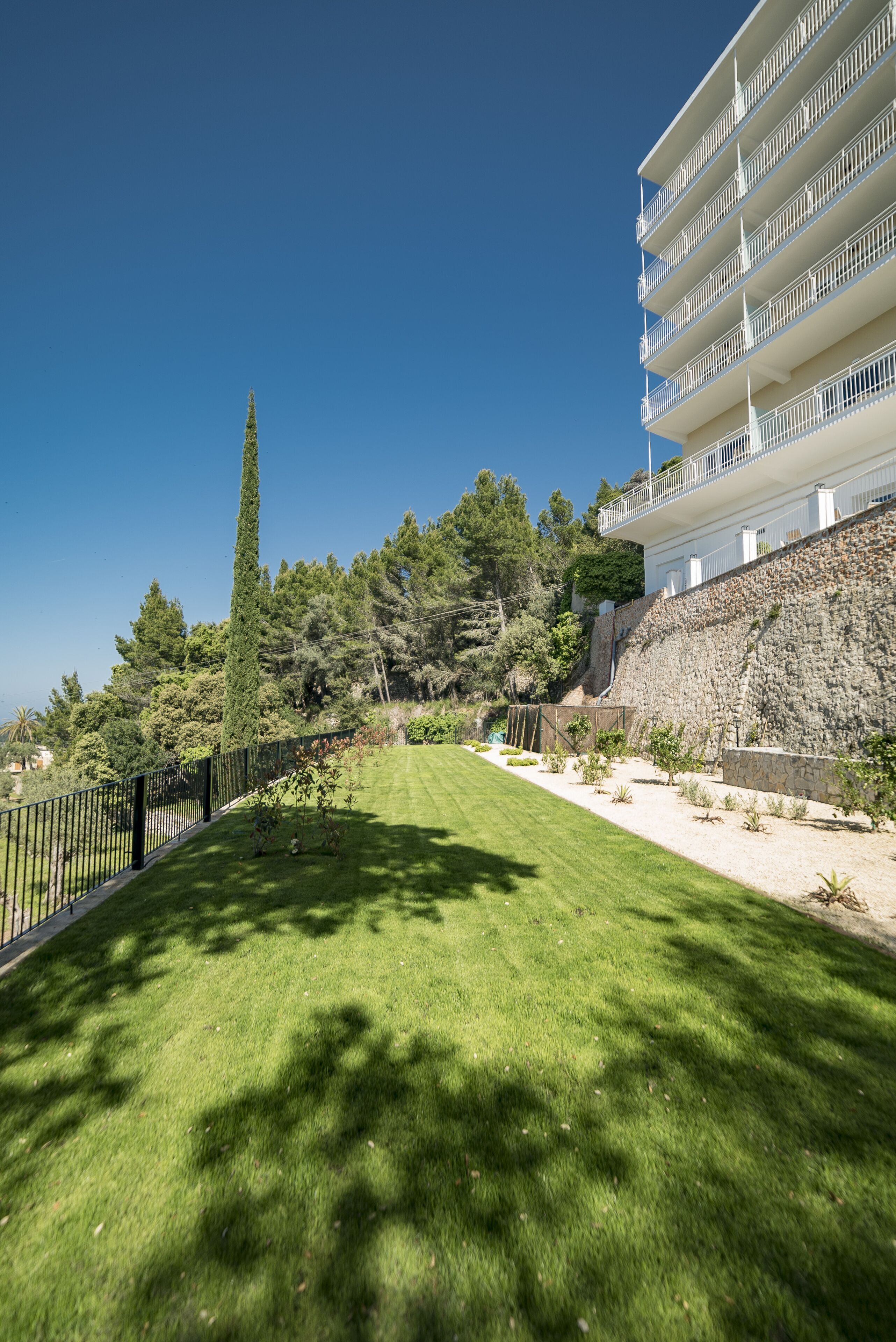 A well-maintained lawn, a stone retaining wall, and a multi-story building with balconies.