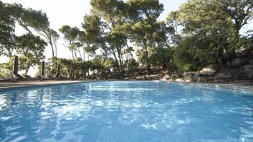 Una piscina con suelo de baldosas, rodeada de árboles y rocas.
