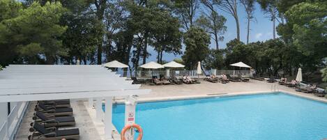 A pool area with sun loungers and umbrellas, surrounded by trees.