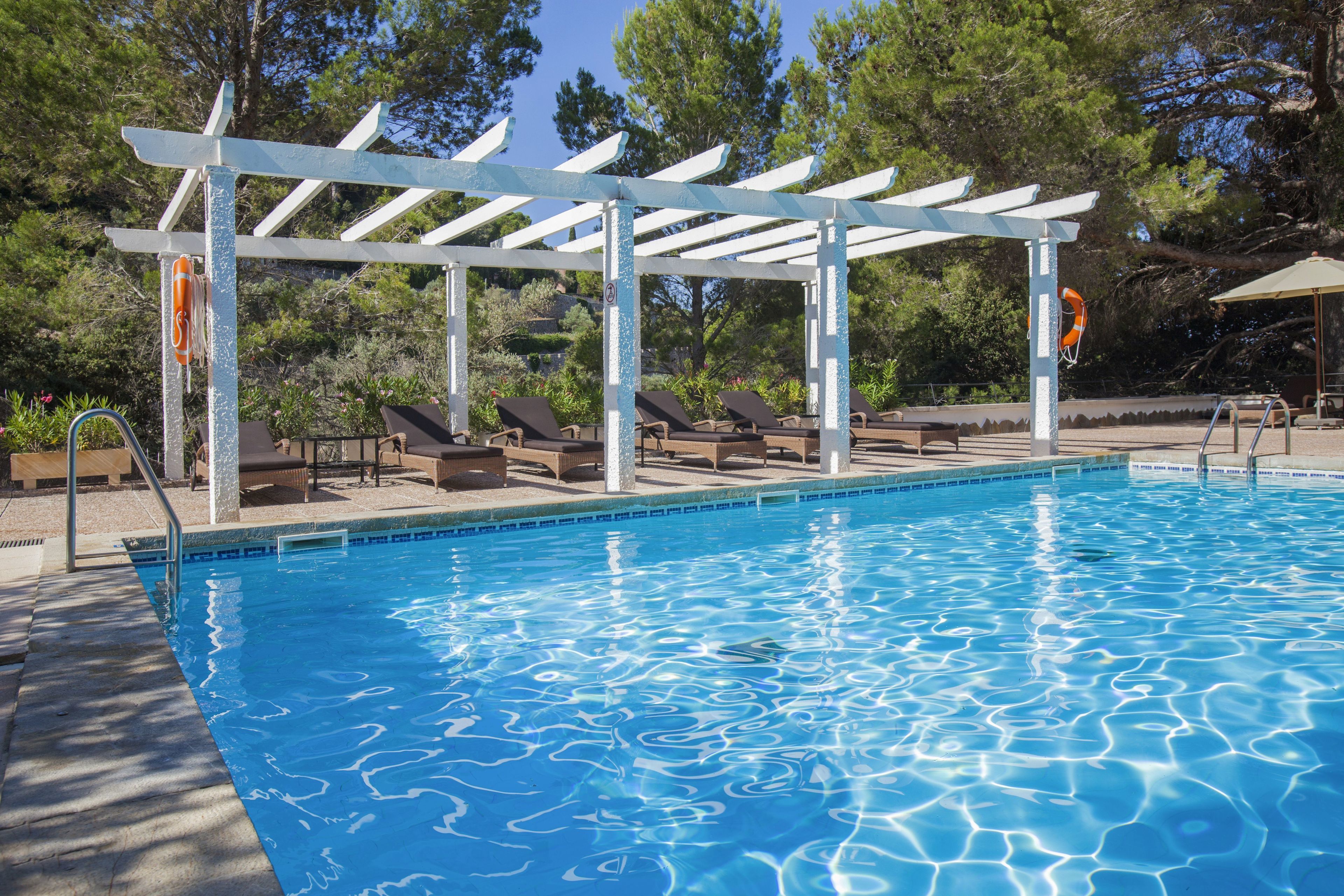 Una piscina con un pérgola y sillones de descanso.