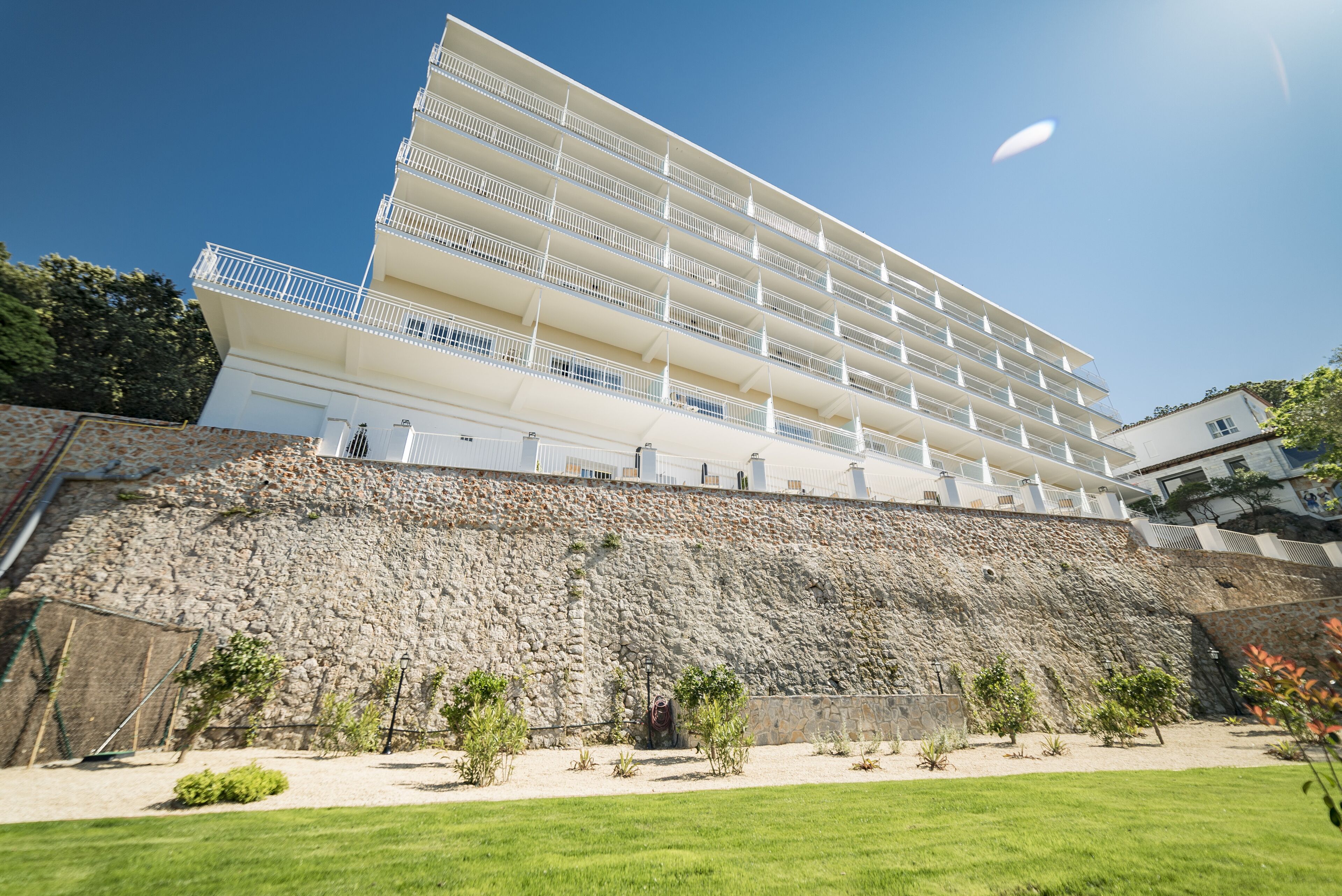 A multi-story hotel with balconies, a stone retaining wall, and a grassy courtyard.