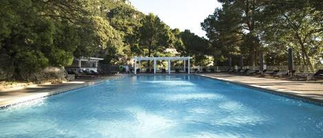 A swimming pool with a white gazebo in the center, surrounded by trees and a mountain backdrop.