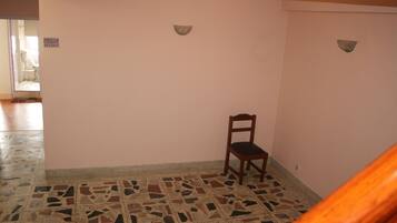 Una habitación con piso de baldosas, una silla de madera y una lámpara fijada a la pared.
