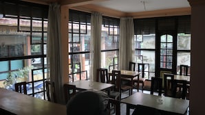 A restaurant with large windows, wooden tables, and chairs. - Om Tara Guest House (Kathmandu)
