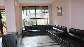 A living room with a sectional sofa, a radiator, and a large window with a view of buildings outside. - Om Tara Guest House (Kathmandu)