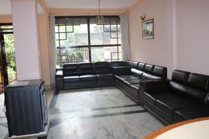 Ein Wohnzimmer mit Ecksofa, Heizkörper und großem Fenster mit Blick auf Gebäude.