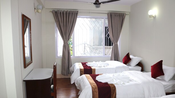 A hotel room with two beds, a desk, and a window with curtains. - Om Tara Guest House (Kathmandu)
