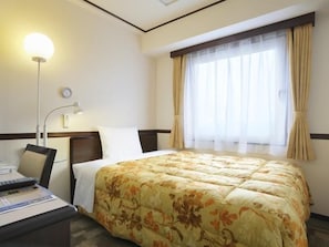 A hotel room with a bed, a desk with a lamp, a window with curtains, and a wall clock.