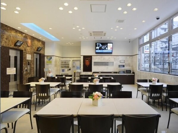 A restaurant with multiple tables, a TV screen, and a view of the city through large windows.